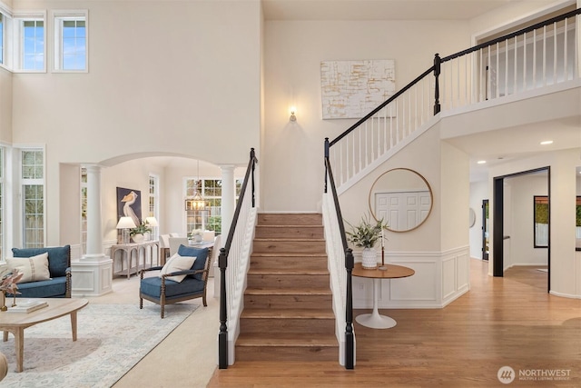 stairway featuring hardwood / wood-style flooring, a high ceiling, and ornate columns