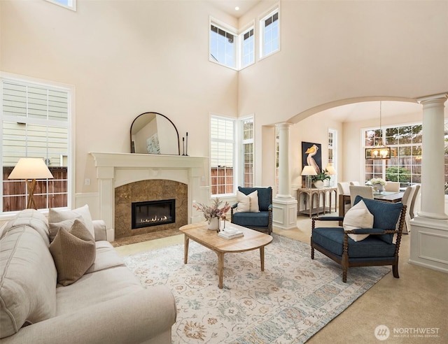 living room featuring decorative columns, a premium fireplace, light colored carpet, and a notable chandelier