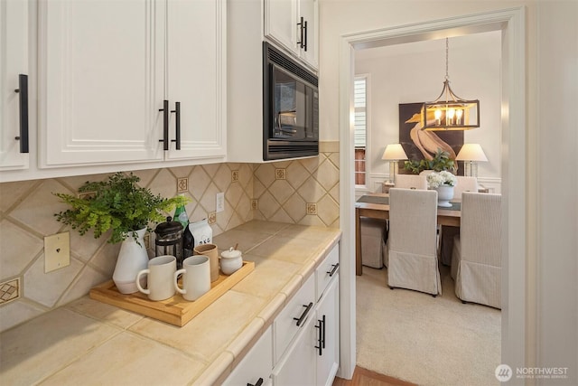 kitchen with an inviting chandelier, decorative light fixtures, black microwave, decorative backsplash, and white cabinets