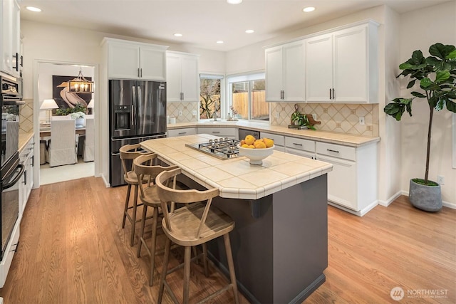 kitchen with white cabinetry, appliances with stainless steel finishes, tile counters, and a kitchen breakfast bar