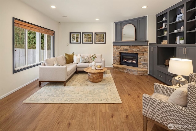 living room featuring built in features, a stone fireplace, and light hardwood / wood-style flooring