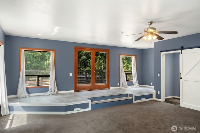 interior space with a barn door, ceiling fan, and dark colored carpet