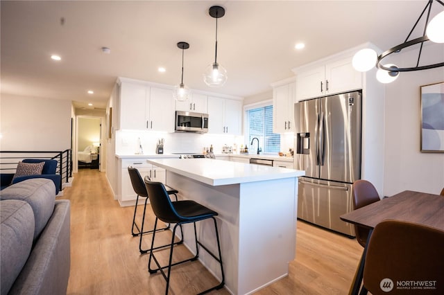 kitchen with a kitchen island, pendant lighting, white cabinetry, light hardwood / wood-style floors, and stainless steel appliances