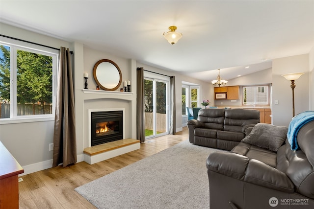 living room with an inviting chandelier, vaulted ceiling, and light wood-type flooring