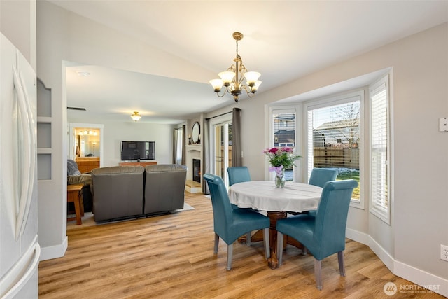 dining room featuring an inviting chandelier, vaulted ceiling, and light wood-type flooring