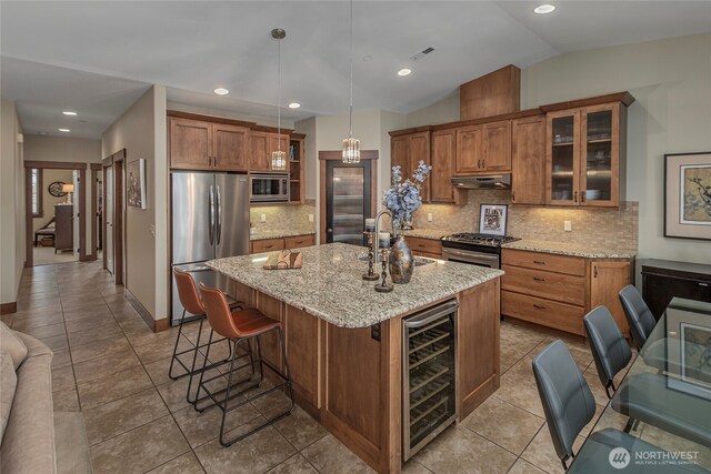 kitchen featuring beverage cooler, under cabinet range hood, brown cabinets, stainless steel appliances, and a sink