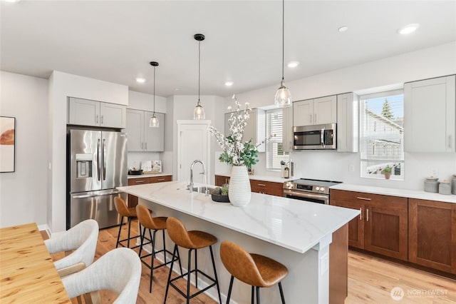 kitchen with light stone counters, pendant lighting, a center island with sink, and appliances with stainless steel finishes