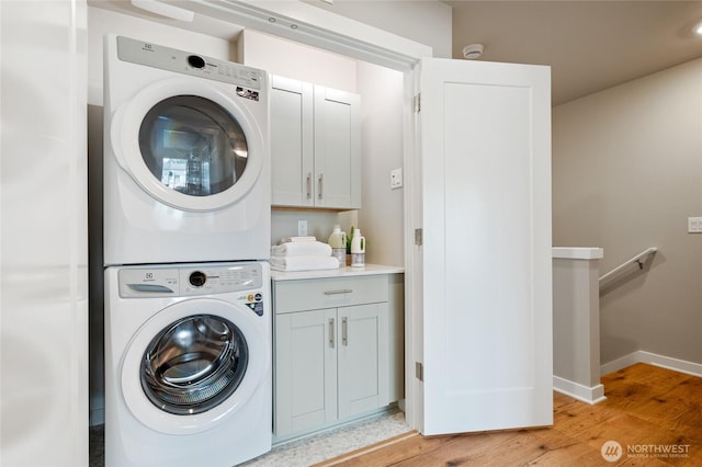 laundry room with stacked washer / drying machine, light hardwood / wood-style floors, and cabinets