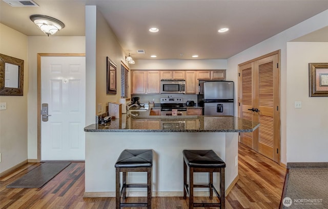 kitchen featuring stainless steel appliances, wood-type flooring, a breakfast bar, and kitchen peninsula