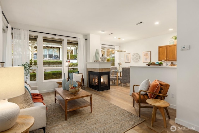 living room featuring light wood finished floors, visible vents, baseboards, a multi sided fireplace, and recessed lighting