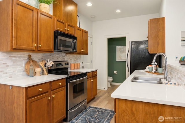 kitchen with brown cabinetry, backsplash, stainless steel appliances, and a sink