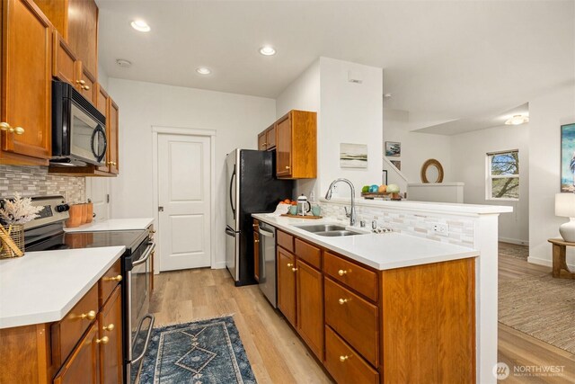 kitchen with a sink, tasteful backsplash, appliances with stainless steel finishes, a peninsula, and brown cabinetry