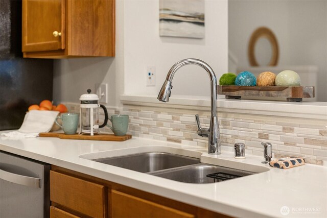 details with a sink, backsplash, stainless steel dishwasher, brown cabinetry, and light countertops