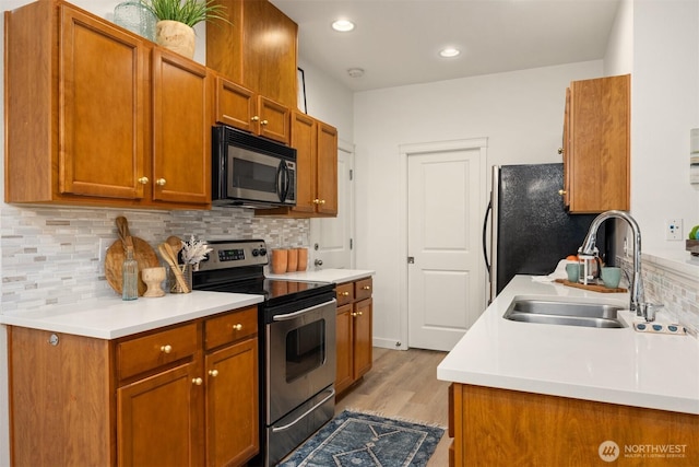 kitchen featuring brown cabinets, a sink, backsplash, appliances with stainless steel finishes, and light countertops