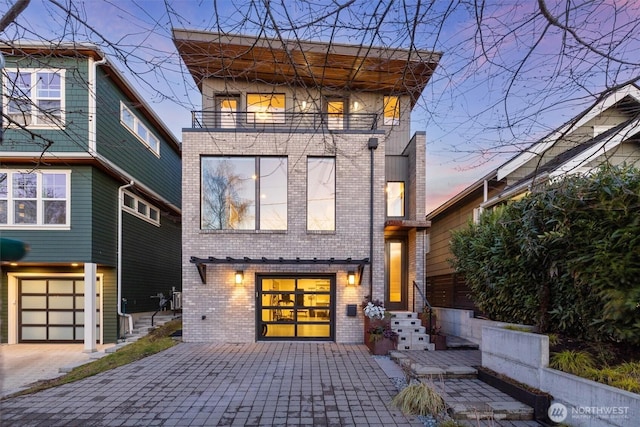 back house at dusk featuring a garage and a balcony