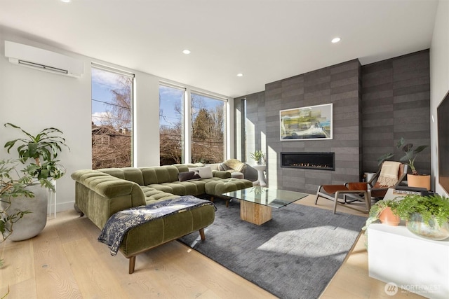 living room with a wall mounted air conditioner, light hardwood / wood-style flooring, and a large fireplace