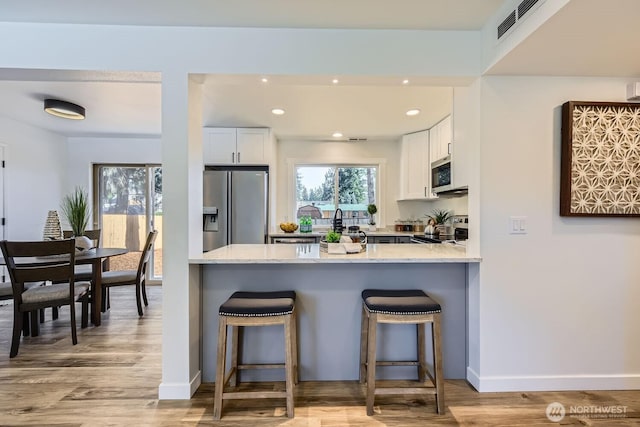 kitchen featuring a breakfast bar area, light hardwood / wood-style flooring, white cabinetry, stainless steel appliances, and light stone countertops