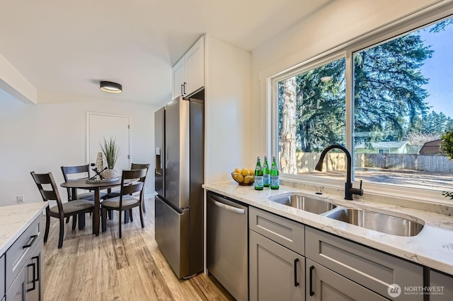 kitchen with sink, light stone countertops, light hardwood / wood-style floors, and appliances with stainless steel finishes