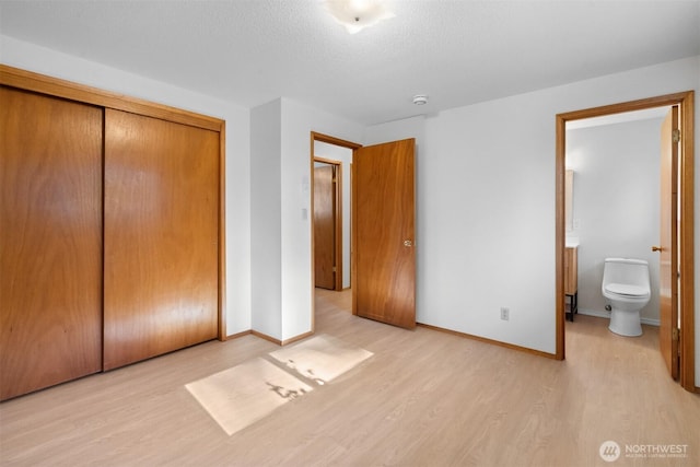 unfurnished bedroom with ensuite bathroom, a textured ceiling, light hardwood / wood-style floors, and a closet