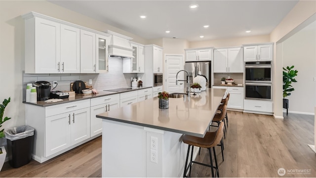 kitchen featuring a kitchen island with sink, stainless steel appliances, white cabinets, a kitchen bar, and light wood-type flooring