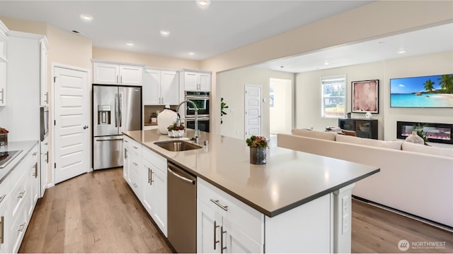 kitchen featuring sink, appliances with stainless steel finishes, a kitchen island with sink, light hardwood / wood-style floors, and white cabinets