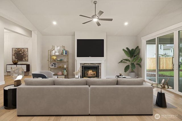 living room with ceiling fan, lofted ceiling, a stone fireplace, and light hardwood / wood-style flooring