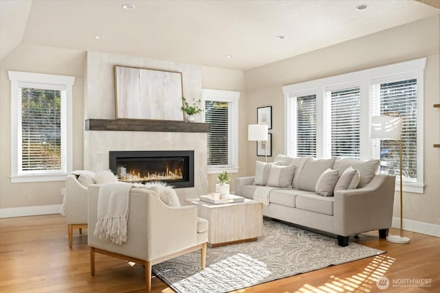 living room featuring recessed lighting, a glass covered fireplace, light wood-style flooring, and baseboards