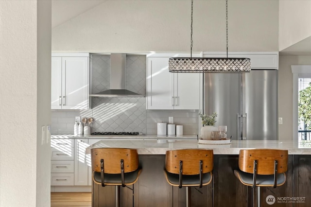 kitchen with tasteful backsplash, a kitchen bar, white cabinets, light stone countertops, and wall chimney exhaust hood