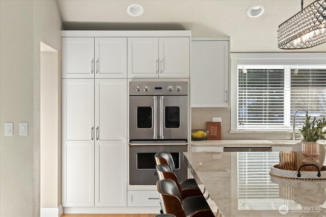 kitchen with light stone countertops, white cabinetry, decorative backsplash, and stainless steel double oven