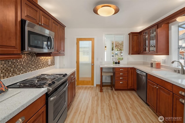 kitchen with appliances with stainless steel finishes, light wood-type flooring, light stone counters, decorative backsplash, and sink