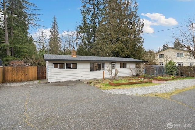 single story home featuring driveway, a chimney, fence, and a garden