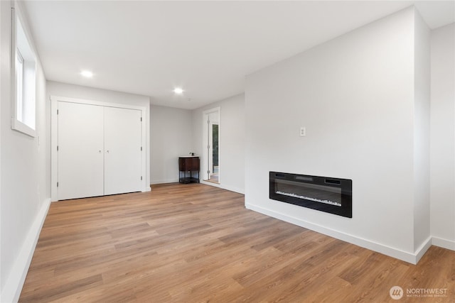 unfurnished living room featuring baseboards, recessed lighting, a glass covered fireplace, and light wood-style floors