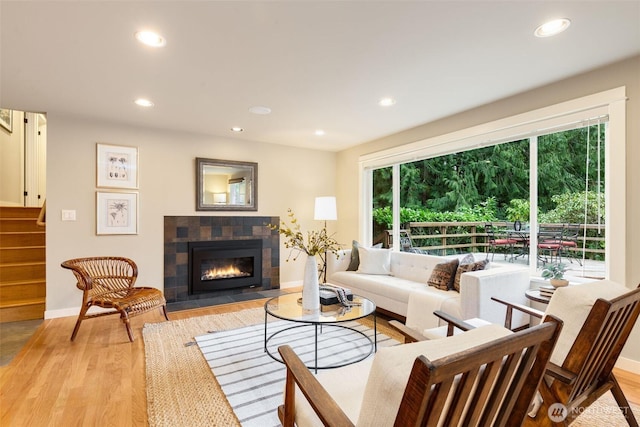 living area featuring light wood finished floors, recessed lighting, a tile fireplace, baseboards, and stairs