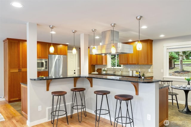 kitchen featuring stainless steel appliances, a kitchen breakfast bar, decorative backsplash, brown cabinets, and island exhaust hood