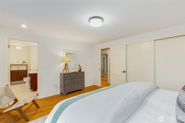 bedroom featuring ensuite bathroom, a closet, light wood-type flooring, and baseboards