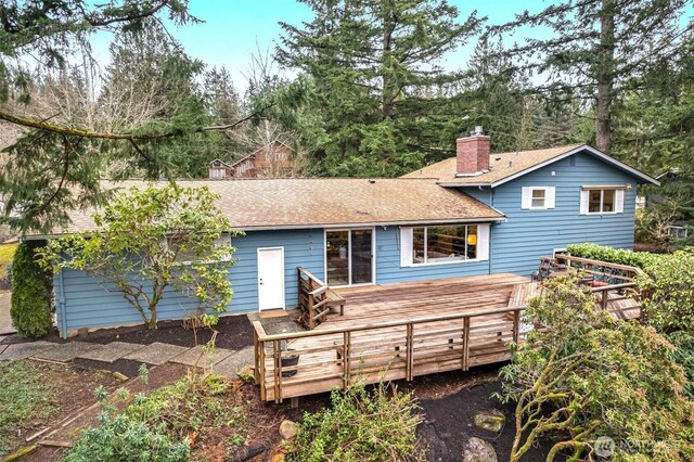 back of house featuring a shingled roof, a chimney, and a wooden deck