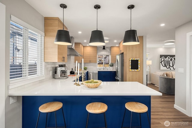 kitchen with appliances with stainless steel finishes, a breakfast bar, wall chimney range hood, and decorative light fixtures