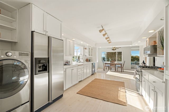 kitchen with appliances with stainless steel finishes, washer / dryer, light hardwood / wood-style flooring, and white cabinets