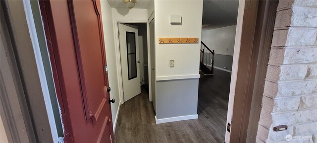 hall with dark wood-type flooring, baseboards, and a textured ceiling