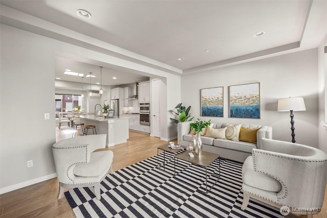 living room featuring a raised ceiling, sink, and light hardwood / wood-style flooring