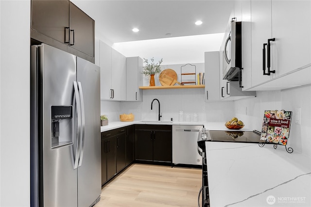 kitchen with appliances with stainless steel finishes, sink, white cabinets, light stone countertops, and light wood-type flooring