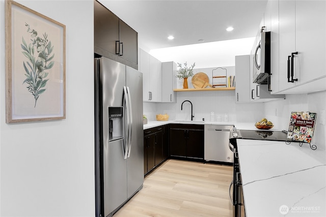 kitchen with light stone counters, appliances with stainless steel finishes, light hardwood / wood-style floors, and sink