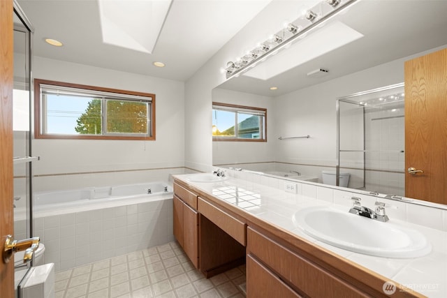 bathroom with a skylight, vanity, a relaxing tiled tub, and toilet