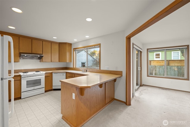 kitchen featuring a breakfast bar, sink, white appliances, kitchen peninsula, and light colored carpet