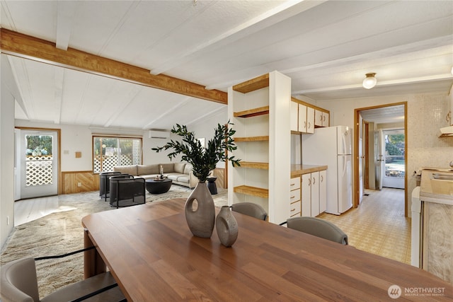 dining room featuring lofted ceiling with beams, a wall mounted AC, and wood walls