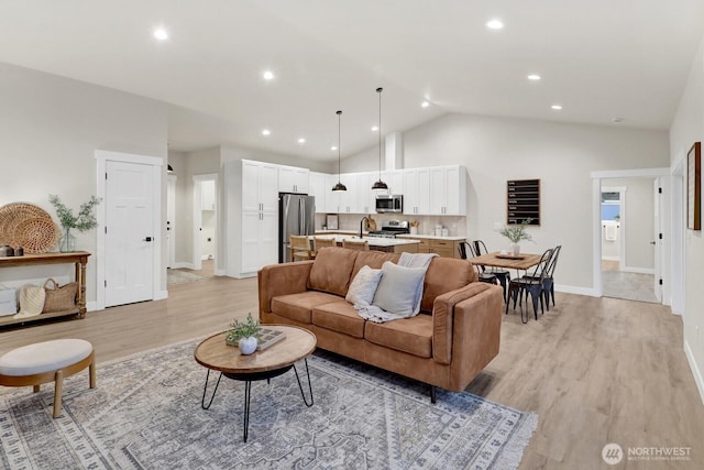 living room featuring vaulted ceiling, sink, and light hardwood / wood-style floors