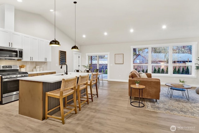 kitchen featuring pendant lighting, a breakfast bar area, a kitchen island with sink, stainless steel appliances, and white cabinets