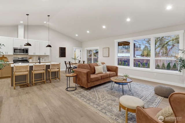 living room with high vaulted ceiling, sink, and light hardwood / wood-style floors