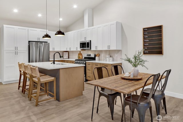 kitchen featuring pendant lighting, sink, white cabinetry, stainless steel appliances, and a center island with sink