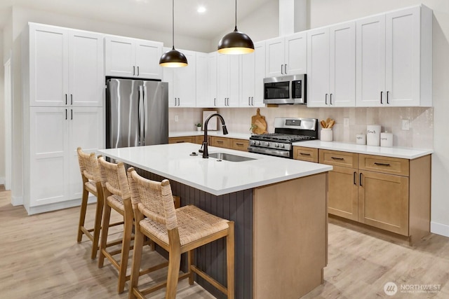 kitchen featuring sink, decorative light fixtures, appliances with stainless steel finishes, an island with sink, and white cabinets